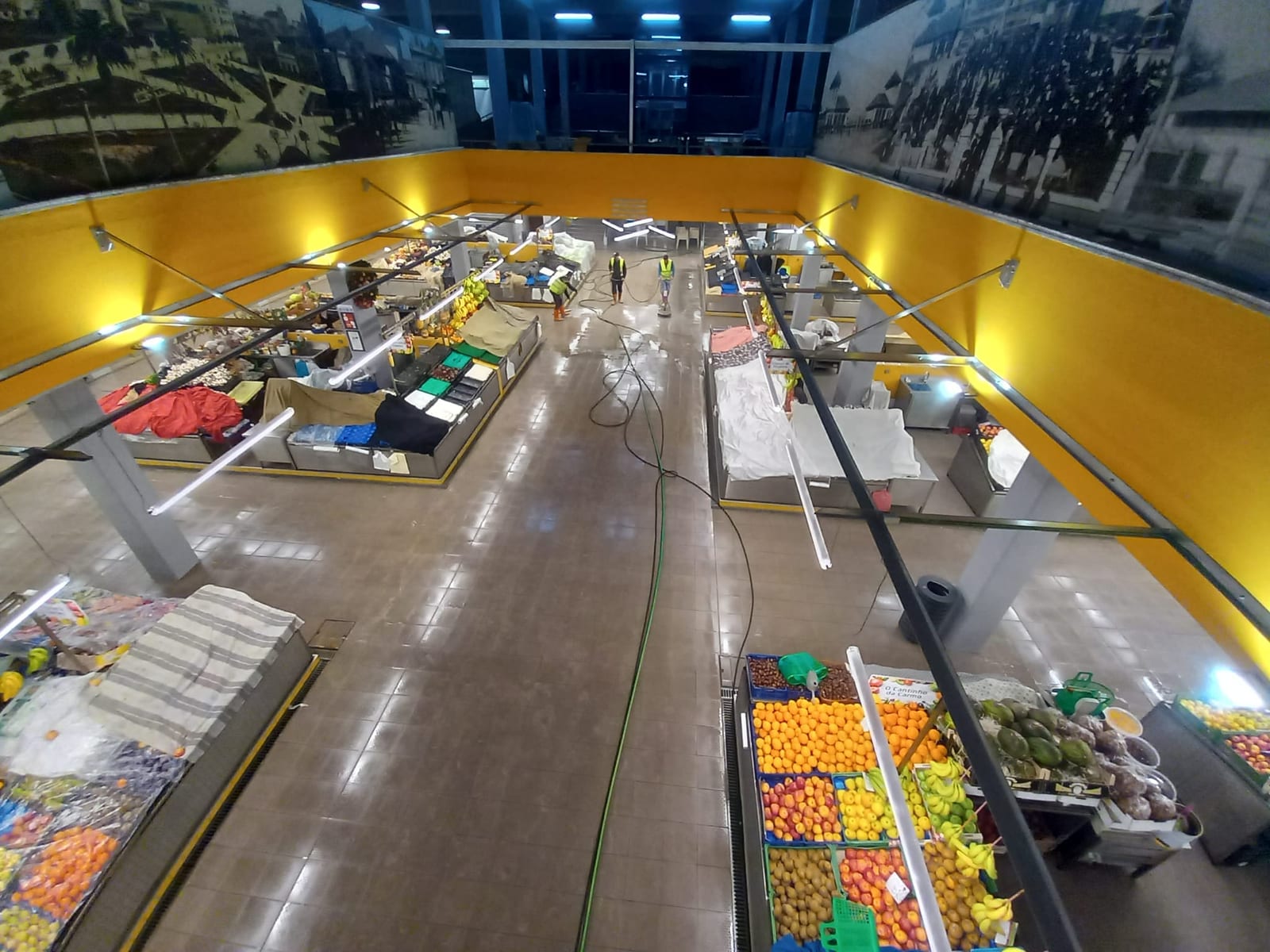 Vista de cima da nave das frutas do Mercado Municipal da Póvoa de Varzim com quatro técnicos a lavar o pavimento.