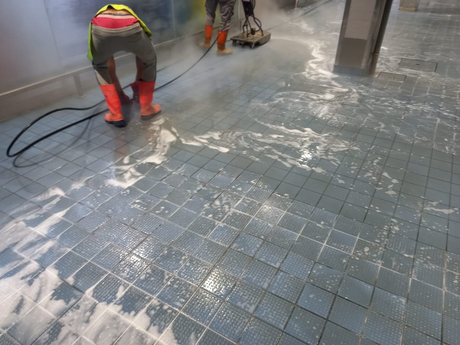 Dois técnicos a lavar pavimento cerâmico azul com espuma, um com escova e outro com máquina rotativa.
