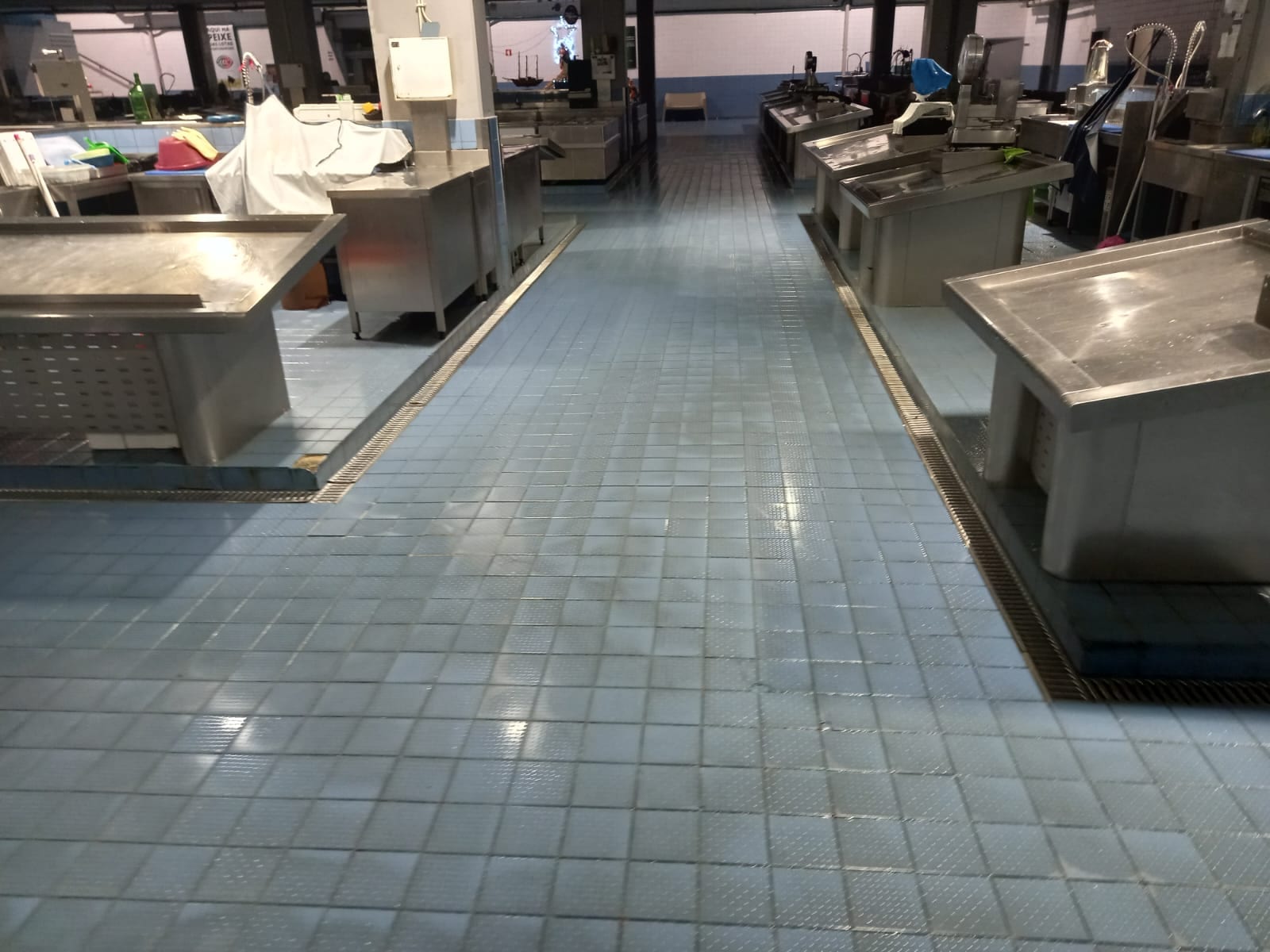 Corredor entre bancas de inox com pavimento cerâmico azul limpo após a lavagem.