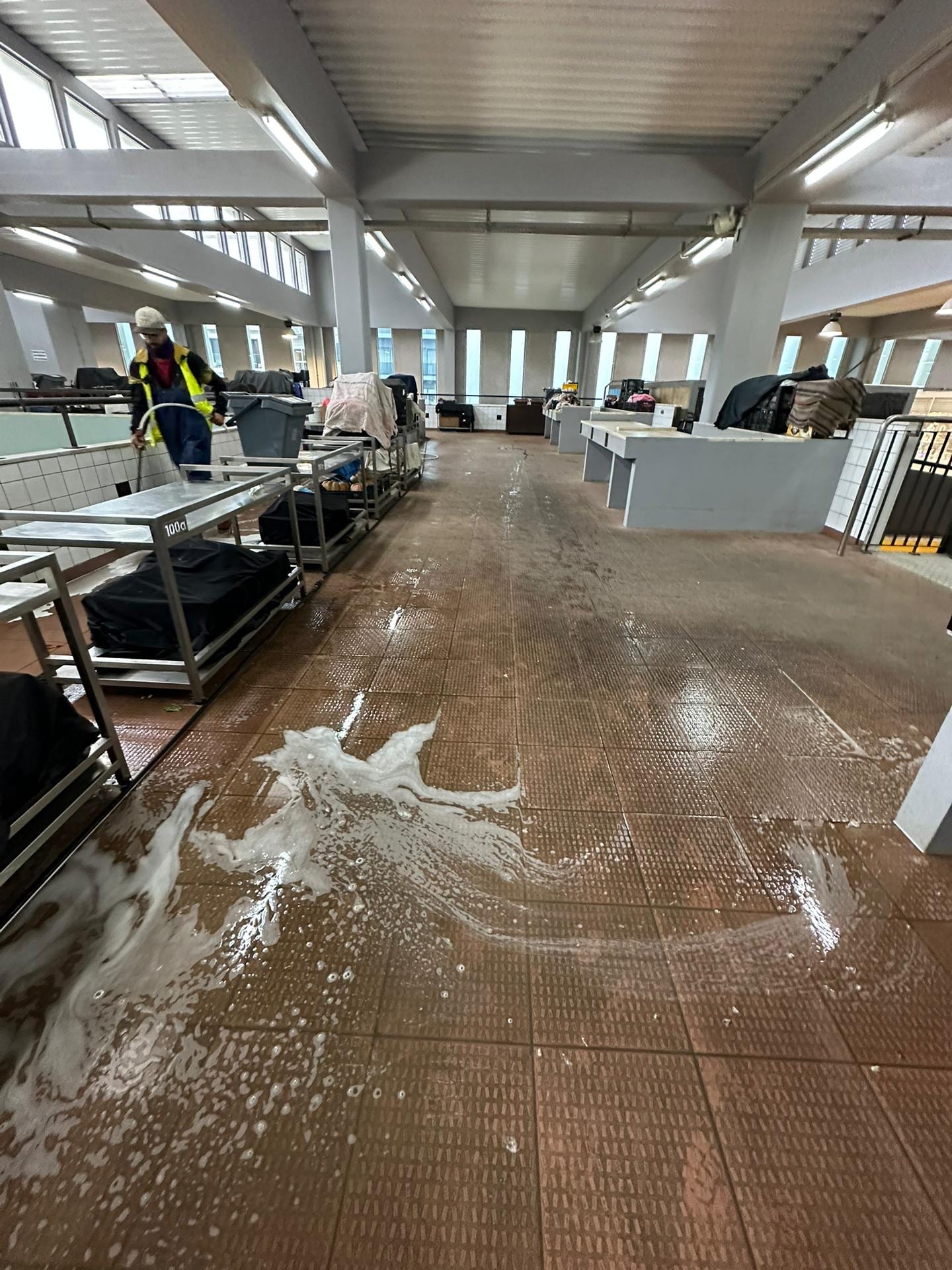 Pavimento cerâmico com espuma durante a lavagem, com um técnico ao fundo.