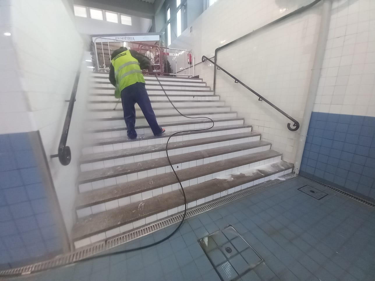 Técnico de colete refletor a lavar as escadas interiores do mercado.
