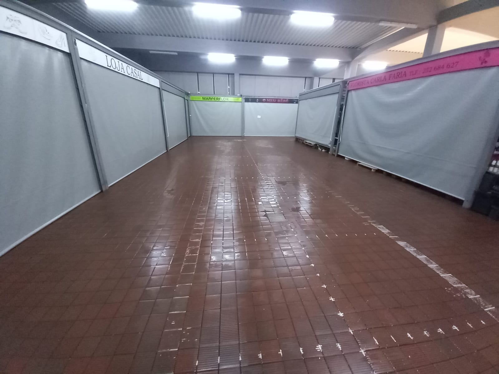 Pavimento cerâmico vermelho lavado numa zona de lojas com cortinas cinzentas.