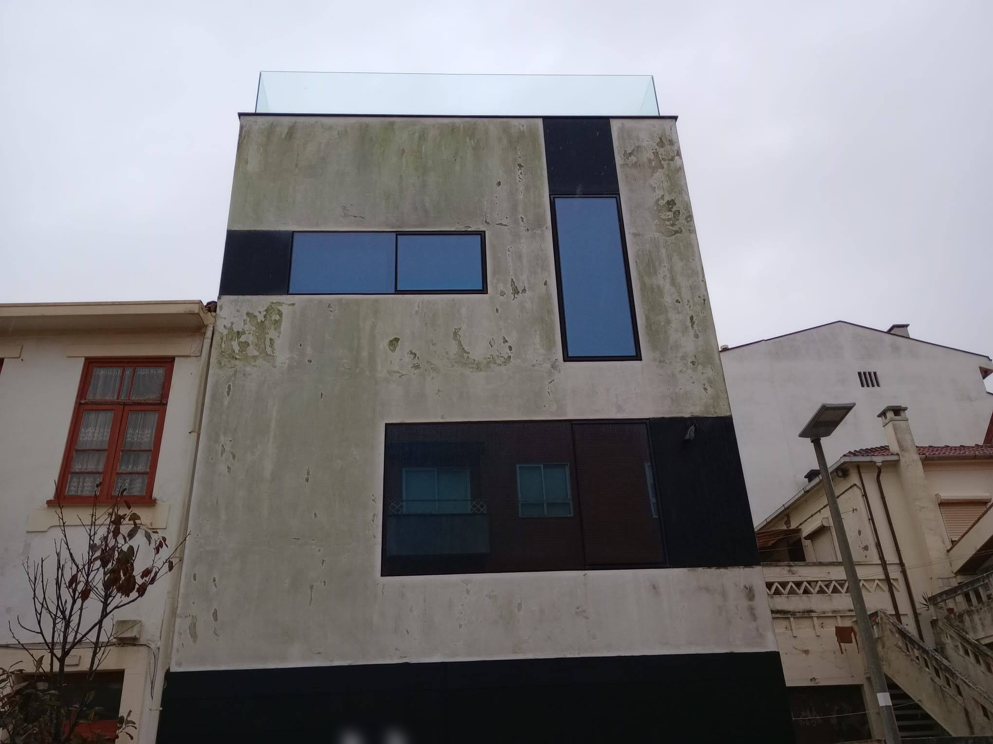 Fachada de moradia com paredes manchadas de verdete e escorrências escuras.