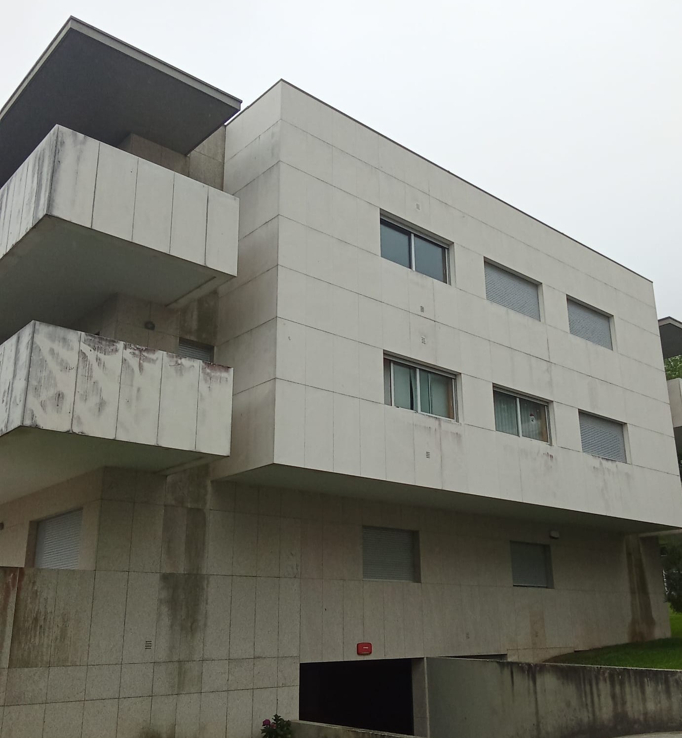 Fachada de condomínio em Viana do Castelo, com paredes manchadas de verdete e escorrências.