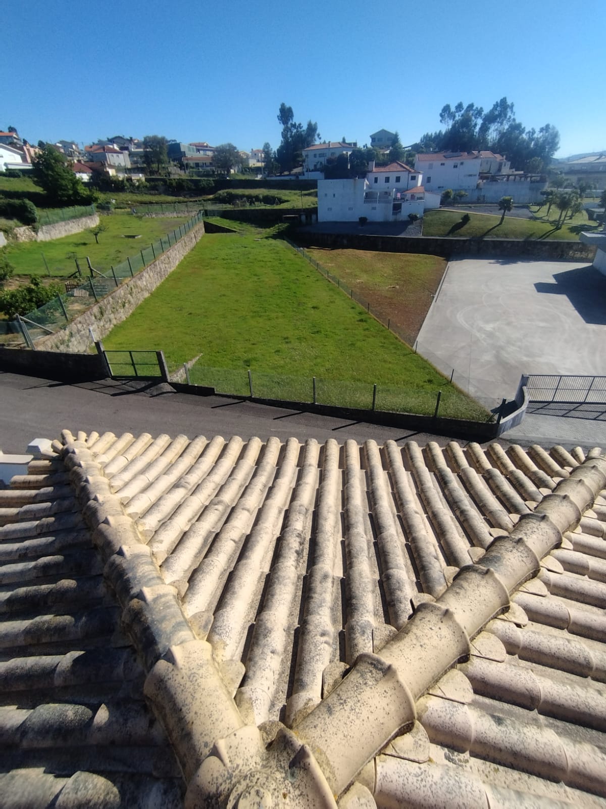 Telhado de moradia com telhas cerâmicas escuras, manchas e musgo nos encontros.