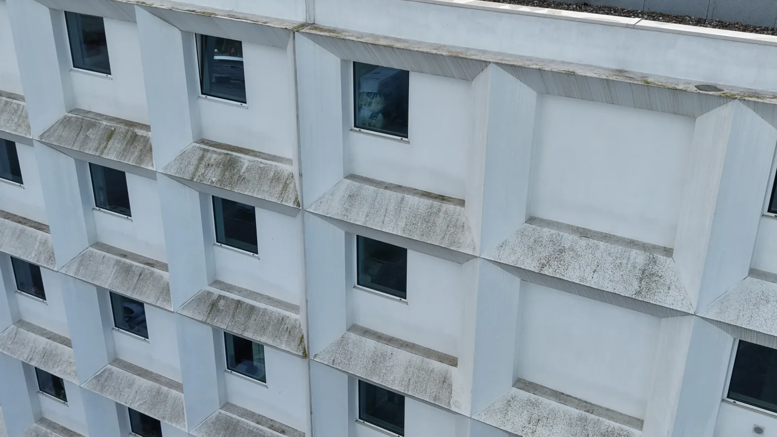 Vista aérea diagonal da fachada branca em módulos salientes do Hotel B&B Vila do Conde antes da lavagem, com parapeitos manchados de verdete