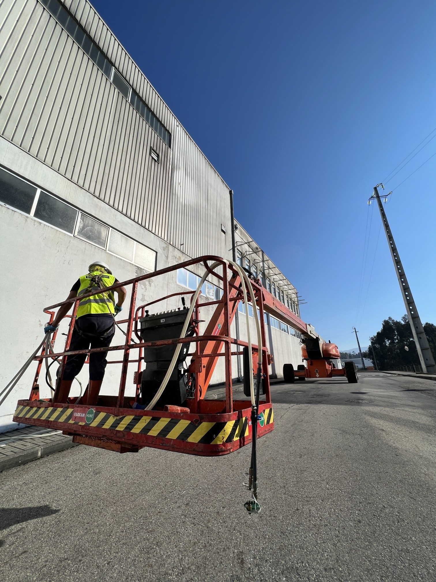 Operador com capacete, colete e arnês numa plataforma elevatória articulada junto à fachada da Bel em Vale de Cambra