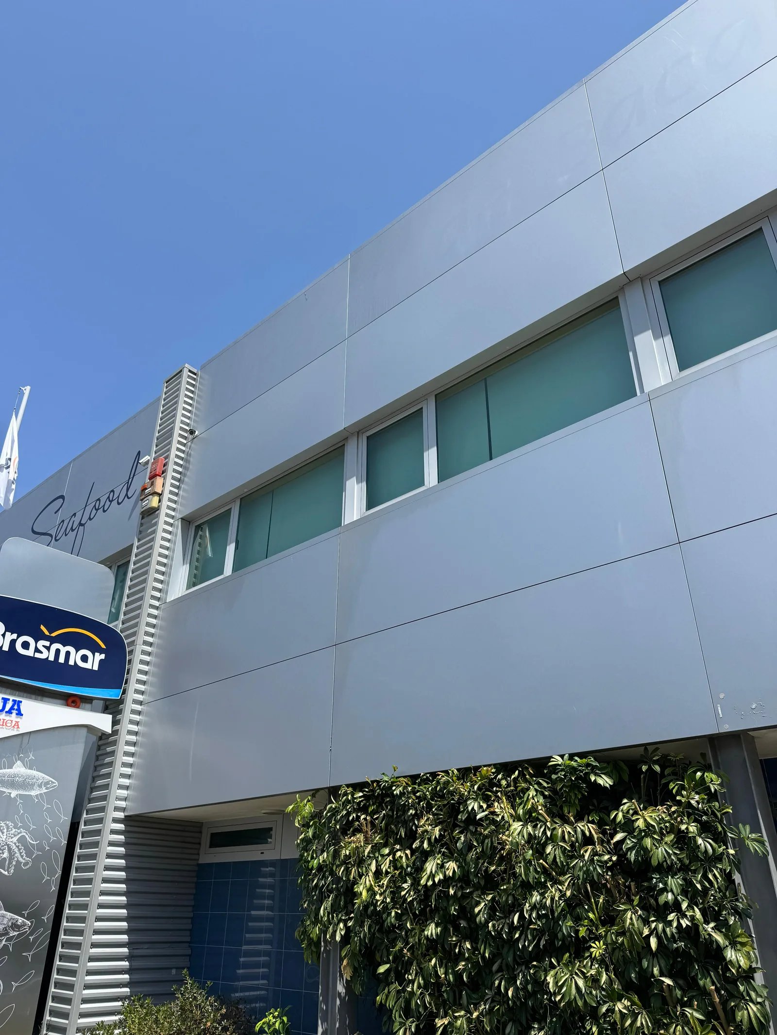 Fachada em chapa canelada da Brasmar com a placa Cais 2, contentor técnico e relva