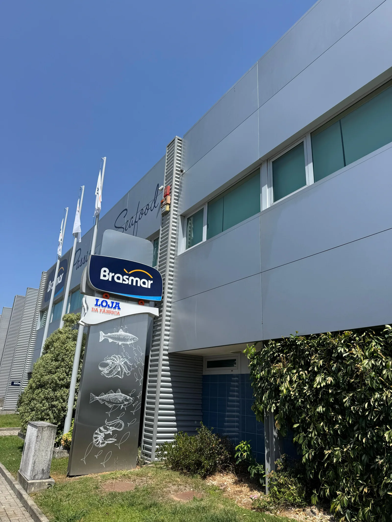 Fachada em chapa canelada da Brasmar ao fim do dia, com contentor técnico e placa Cais 2