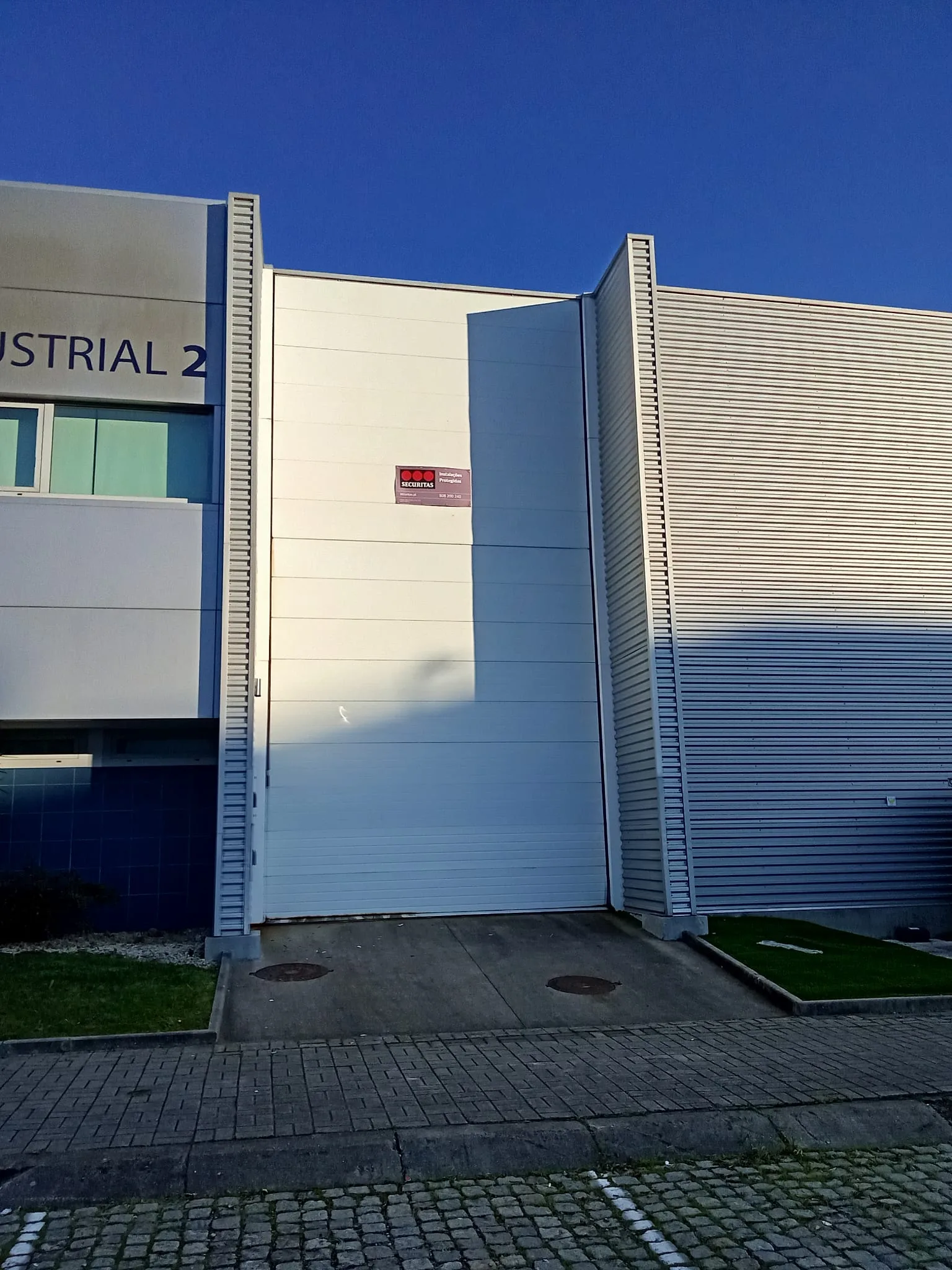 Fachada em chapa canelada da unidade industrial Brasmar em Vila Nova de Famalicão, com porta de serviço e estacionamento