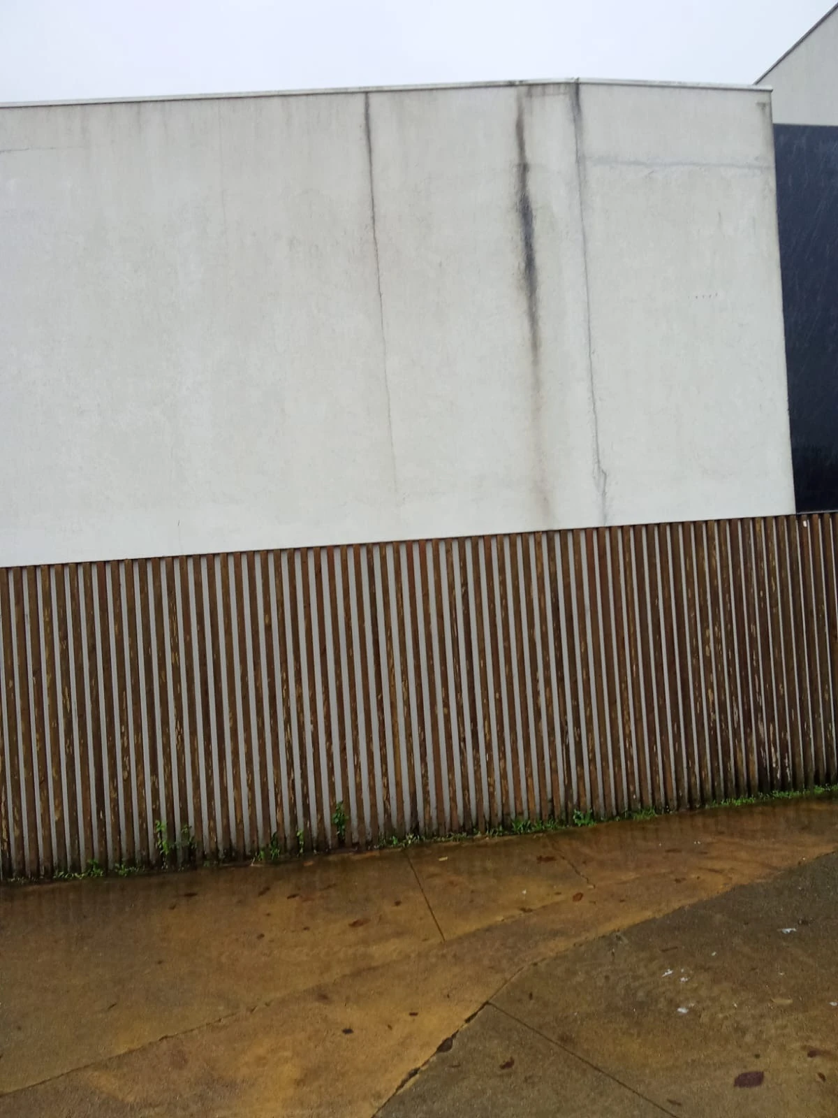 Muro junto à entrada do Fórum Braga com escorridos verticais escuros sobre o ripado, antes da lavagem SoftWash da AREALIMPA