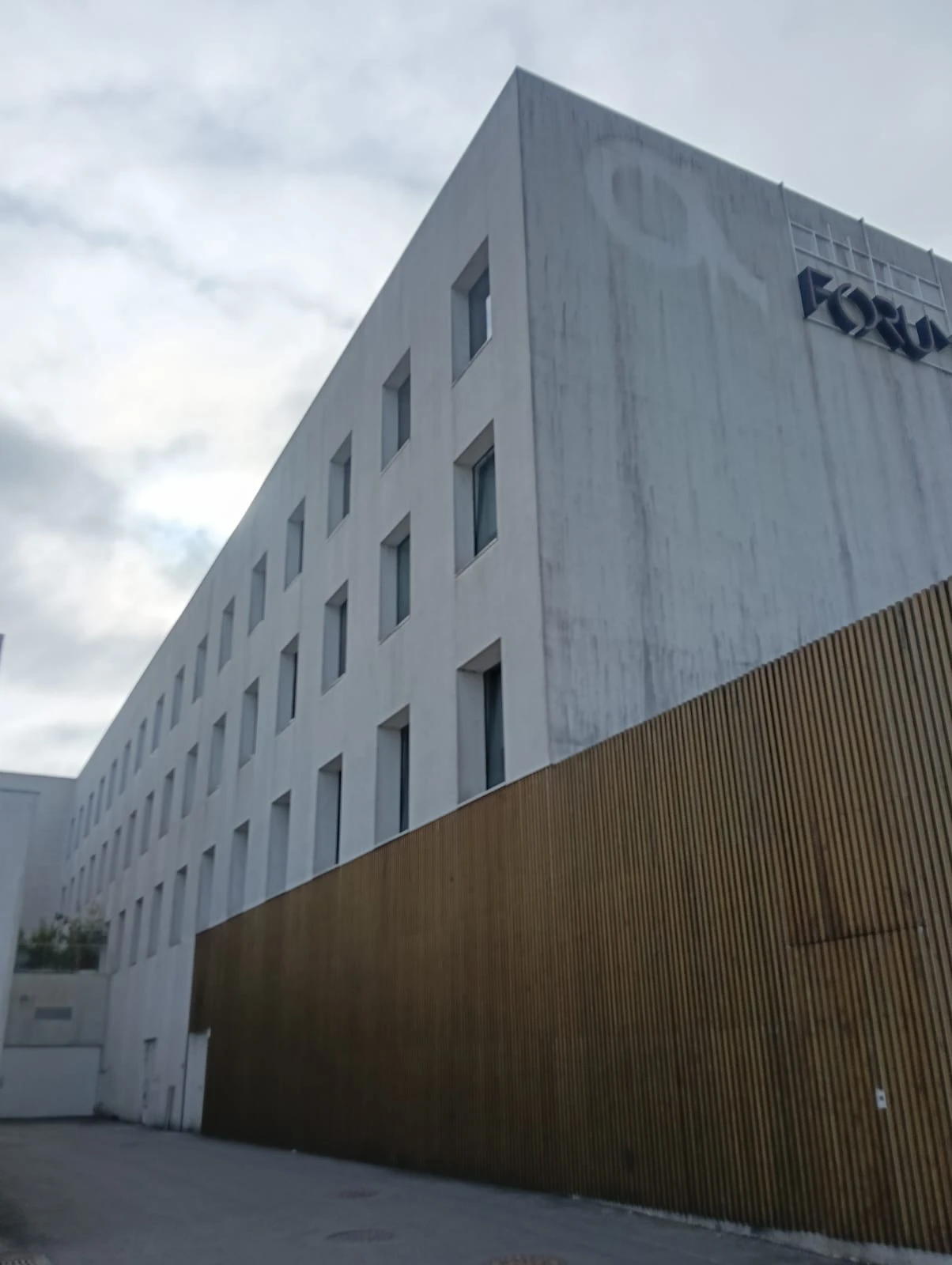 Fachada de quatro pisos do Fórum Braga sobre o ripado de madeira, com manchas escuras e escorridos, antes da lavagem SoftWash da AREALIMPA