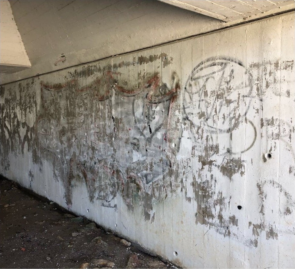 Parede de betão aparente numa passagem coberta em Aveiro com várias camadas de graffiti
