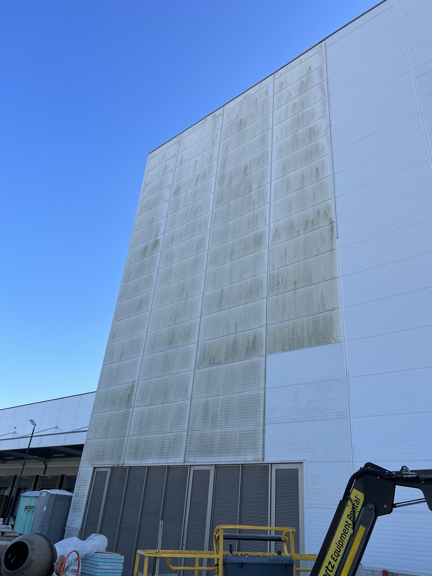 Fachada industrial em painéis de chapa branca em Aveiro com faixas de sujidade verde e uma zona já lavada com SoftWash à direita