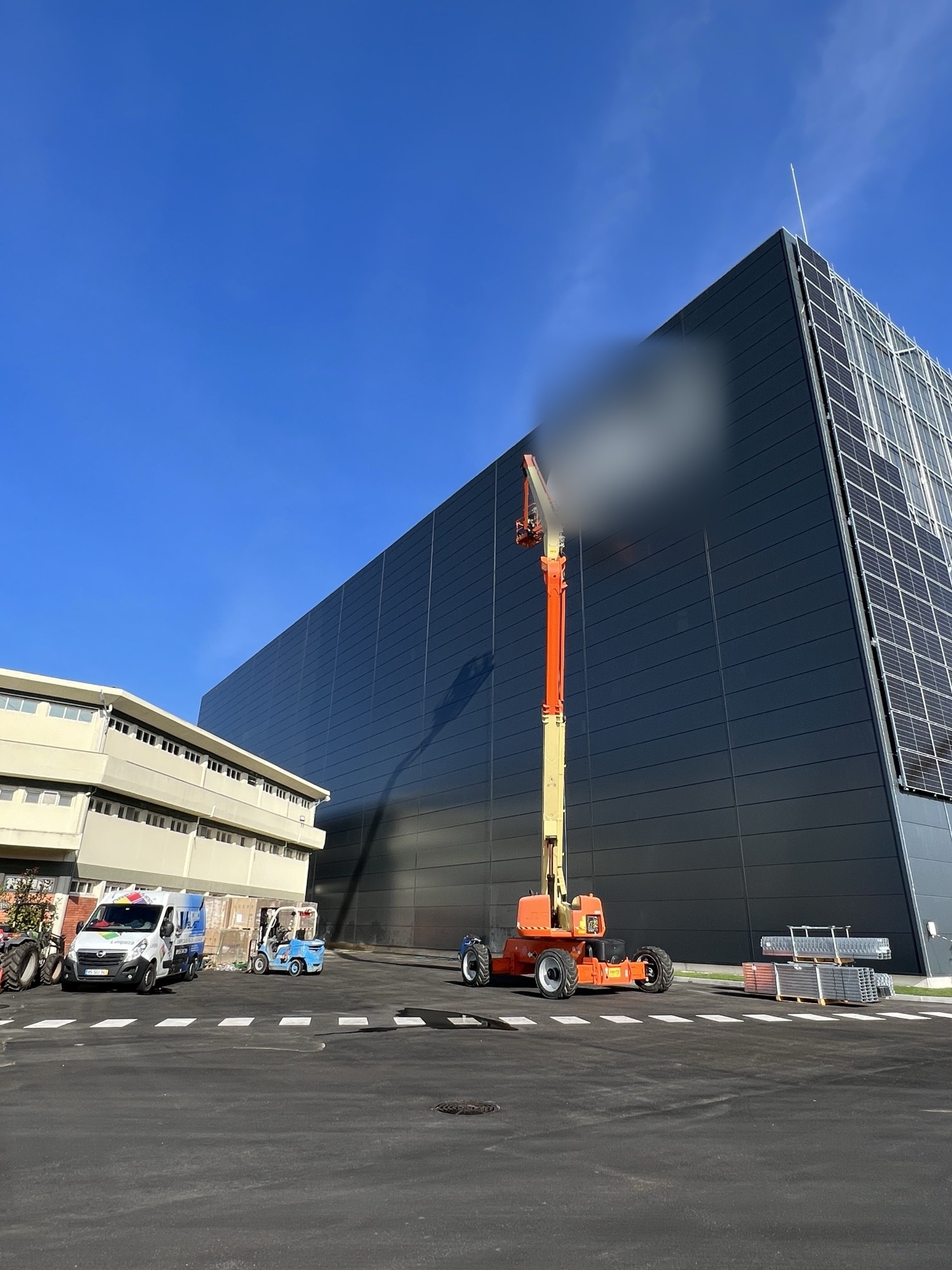 Plataforma elevatória articulada junto à fachada em chapa escura de uma unidade industrial em Aveiro
