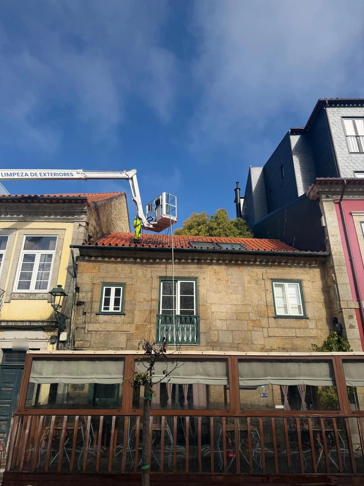 Plataforma elevatória da AREALIMPA posicionada na rua, com o braço estendido sobre o telhado de uma casa em granito no centro de Barcelos