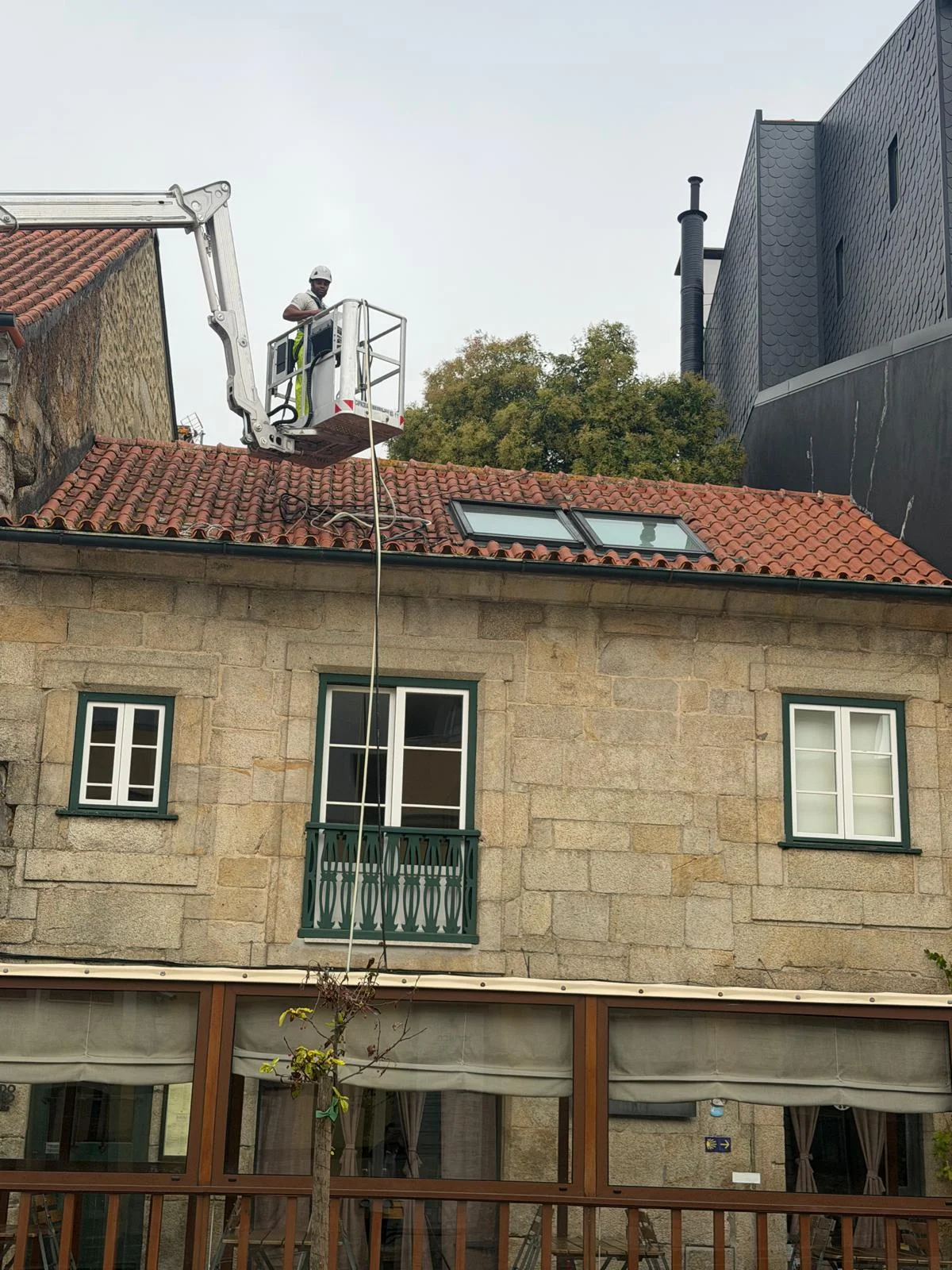 Técnico da AREALIMPA no cesto da plataforma elevatória, por cima do telhado em telha cerâmica