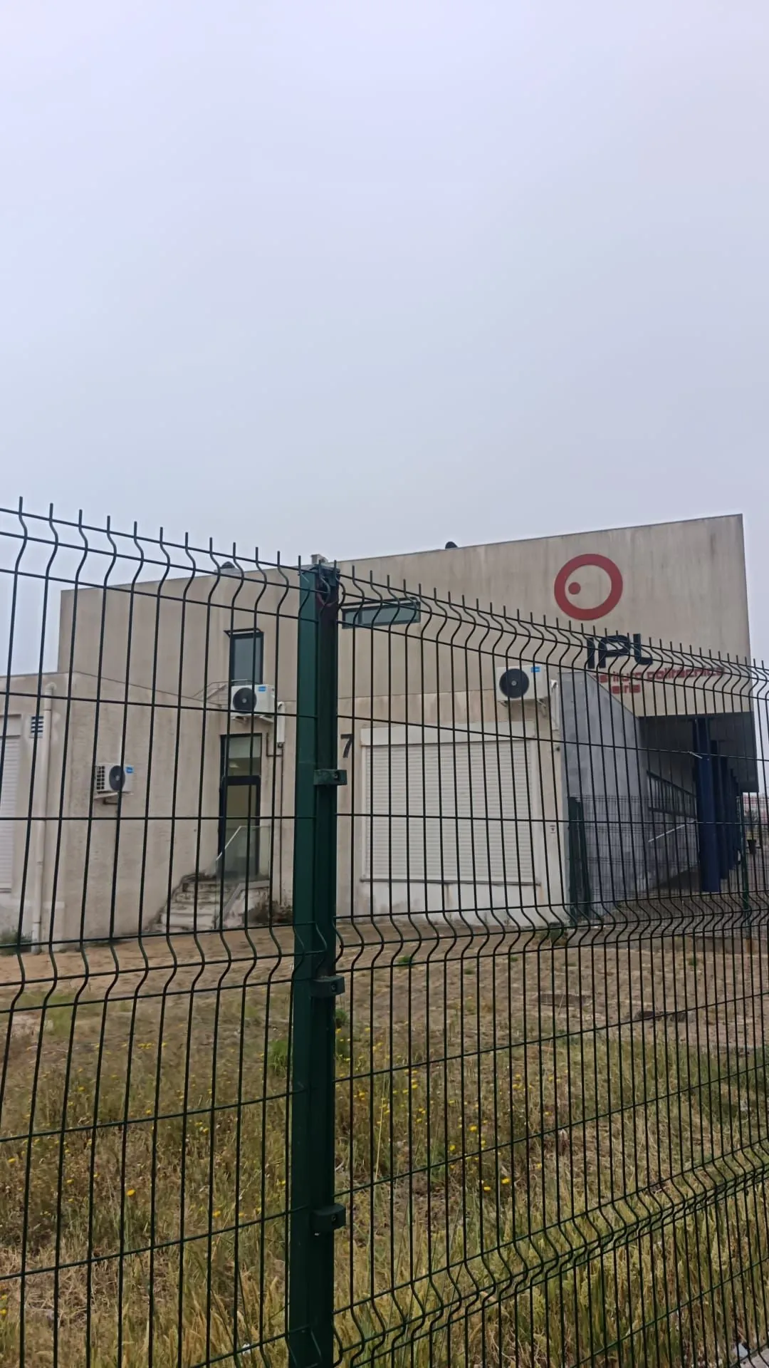 Fachada do Instituto Politécnico de Leiria em Peniche, vista através da vedação, com os planos brancos manchados antes da limpeza da AREALIMPA