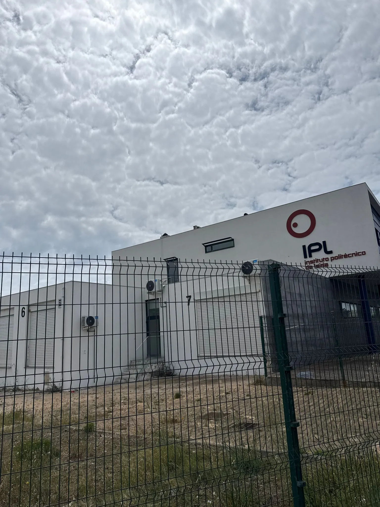 A mesma fachada do Instituto Politécnico de Leiria em Peniche, vista através da vedação, com os planos brancos mais uniformes depois da limpeza da AREALIMPA