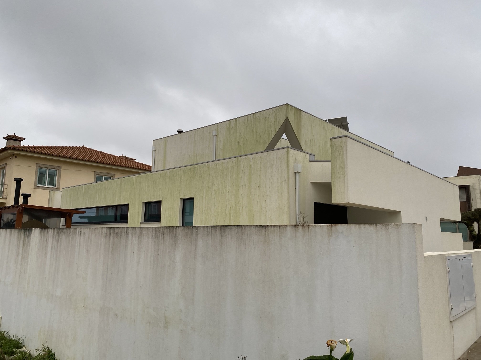 Moradia branca em Aguçadoura, Póvoa de Varzim, com fachadas cobertas de algas verdes antes da limpeza