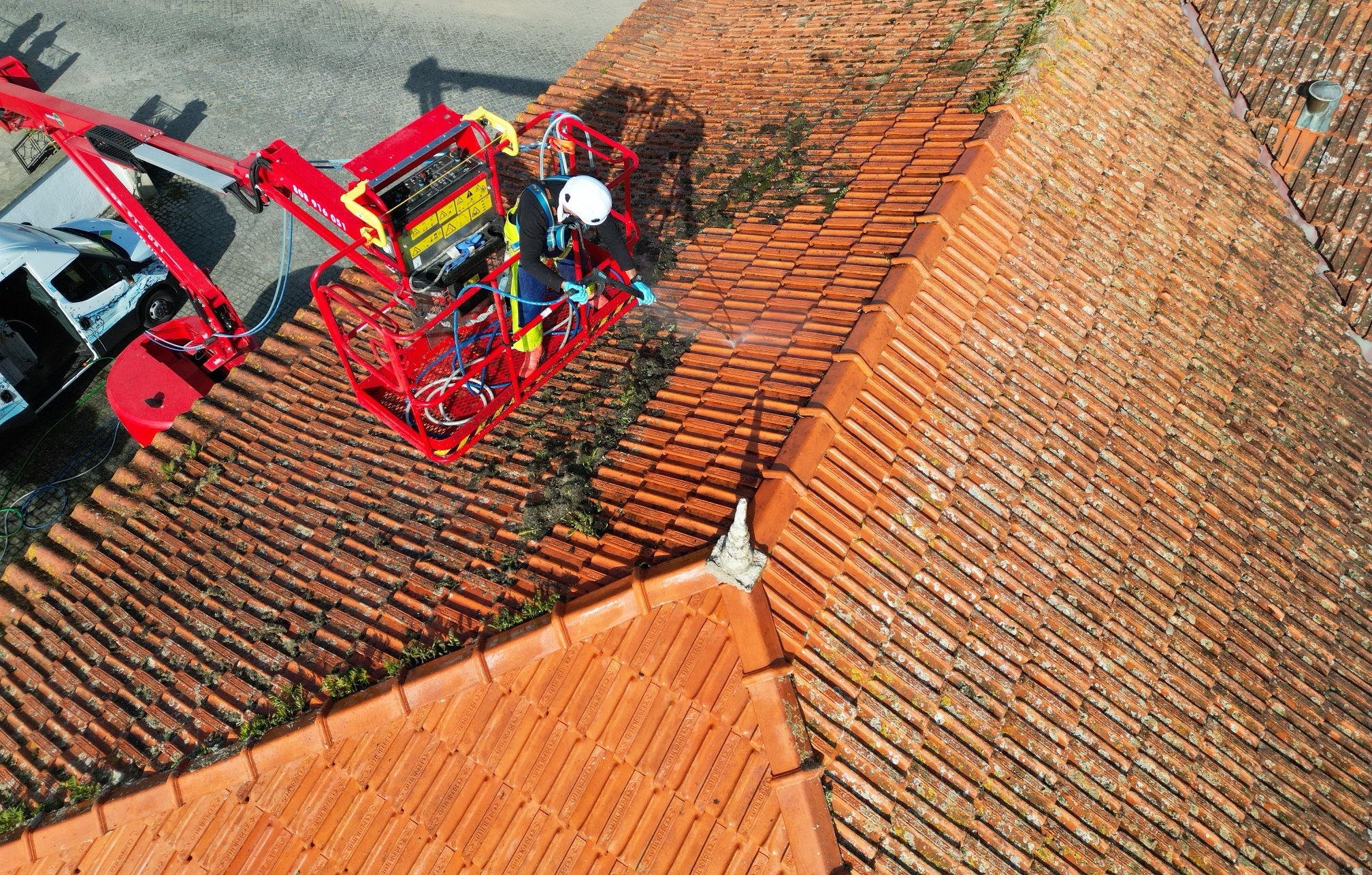 Operador com capacete e arnês numa plataforma articulada a limpar telhado com SoftWash na Póvoa de Varzim